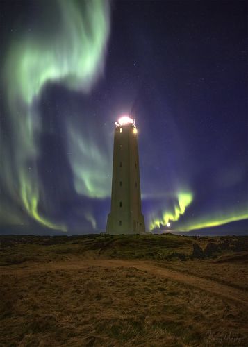 Northern lights dance around lighthouse.